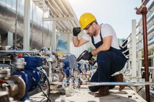 handsome-caucasian-worker-overall-helmet-head-crouching-using-drill-while-crouching-oil-industry