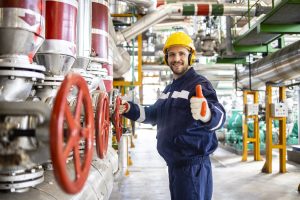 Portrait of heating plant worker engineer standing by natural gas pipelines and holding thumbs up.